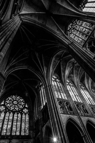 A low angle shot of a cathedral ceiling with windows in black and white