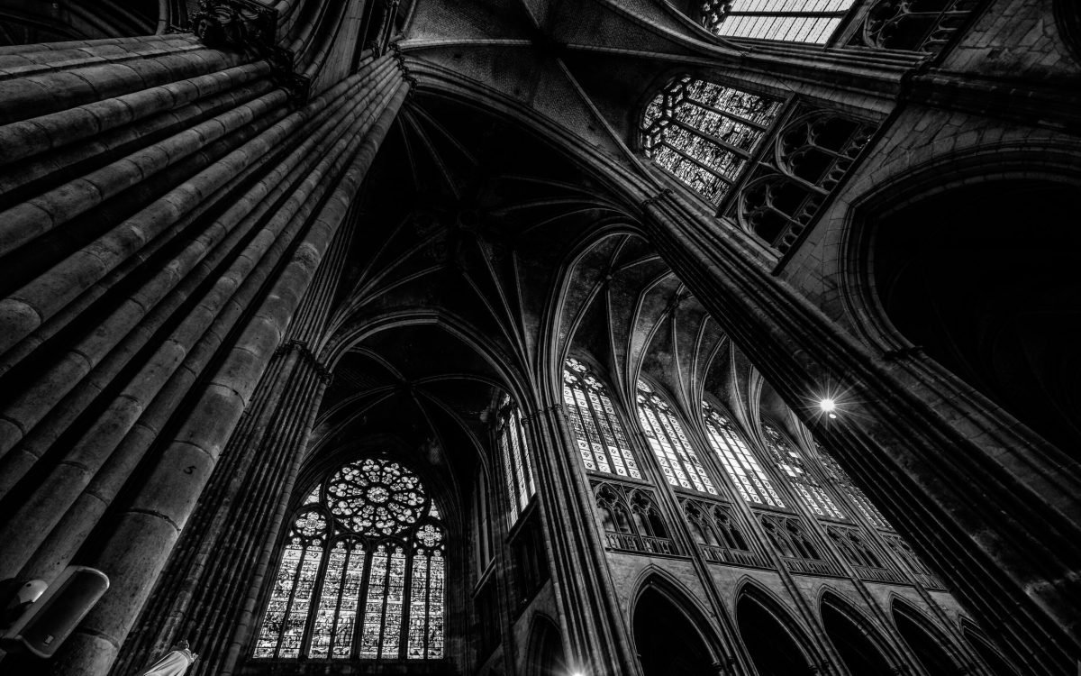 A low angle shot of a cathedral ceiling with windows in black and white
